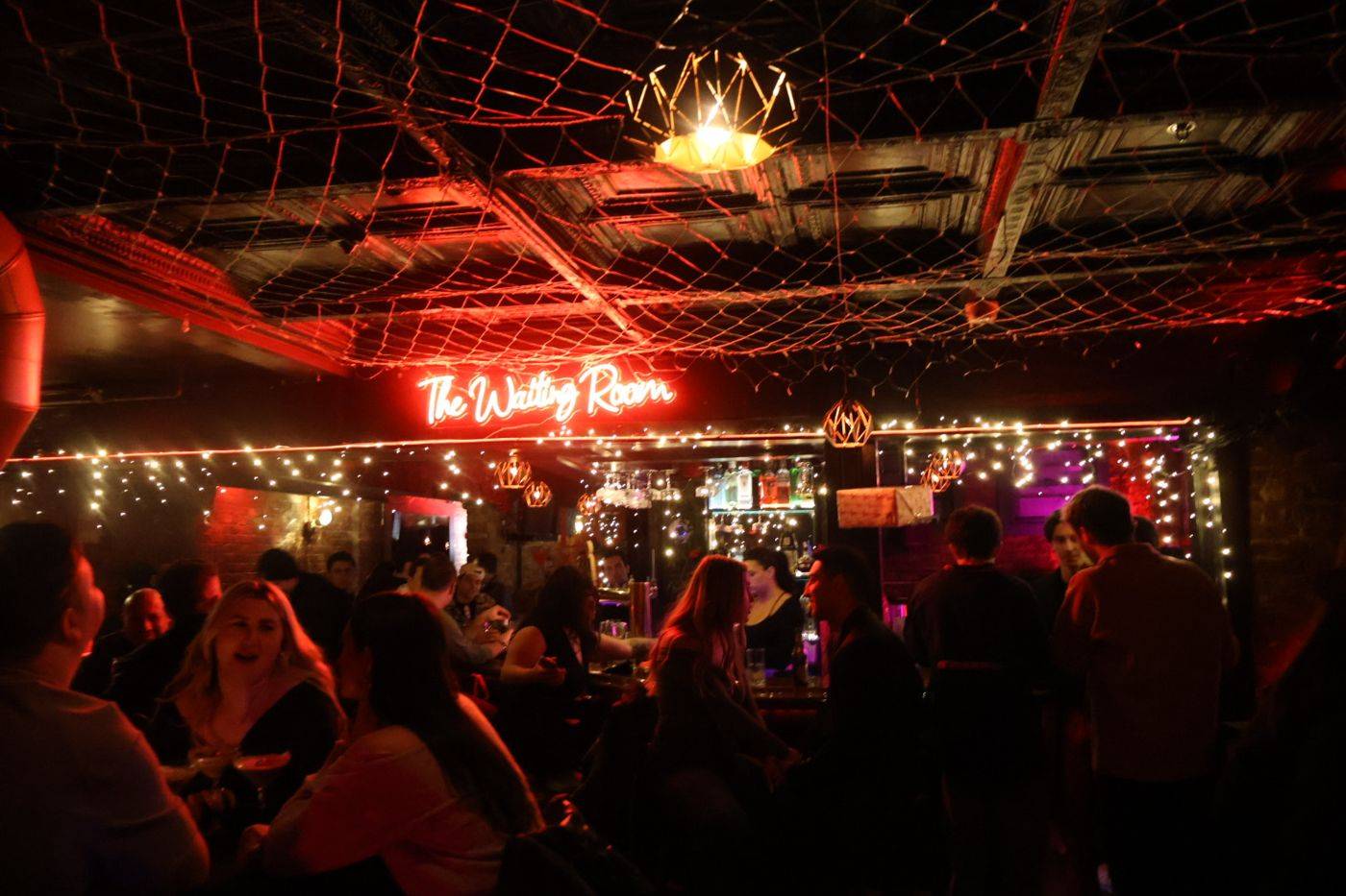 A private party filling The Waiting Room in Hoboken under red neon and string lights
