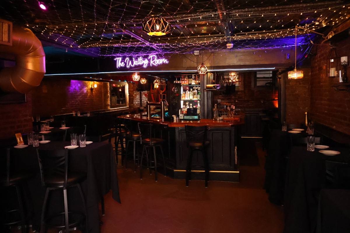 The Waiting Room's main event space in Hoboken set with tables under string lights and neon